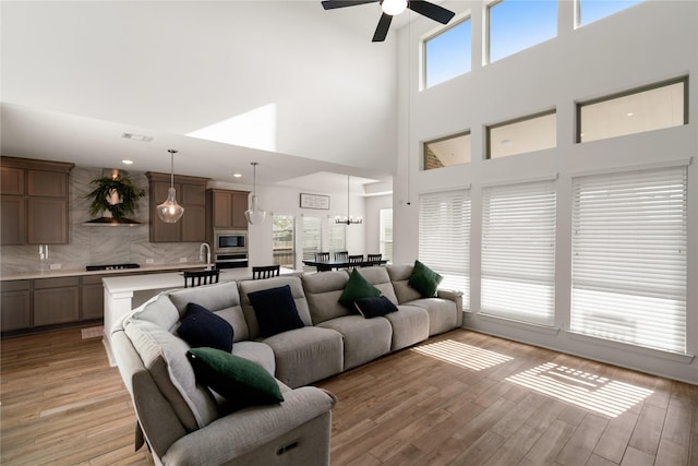 living room featuring ceiling fan with notable chandelier, light hardwood / wood-style flooring, and a high ceiling