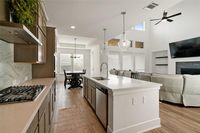 kitchen with sink, wall chimney range hood, ceiling fan, appliances with stainless steel finishes, and hanging light fixtures