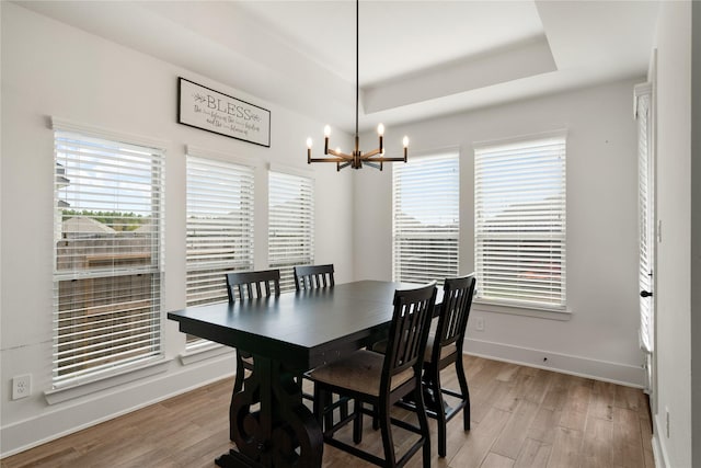 dining area featuring light hardwood / wood-style flooring, a notable chandelier, plenty of natural light, and a raised ceiling