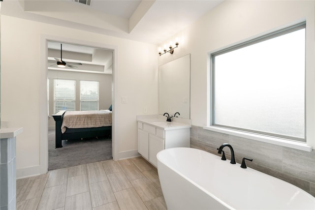 bathroom featuring ceiling fan, vanity, a tray ceiling, and a tub