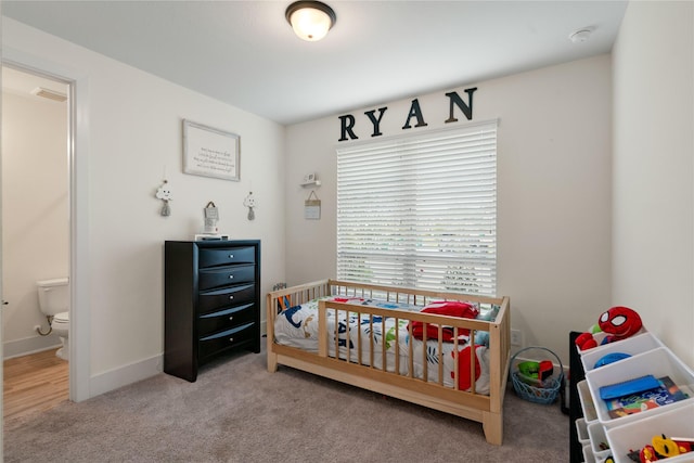 carpeted bedroom featuring connected bathroom and a crib