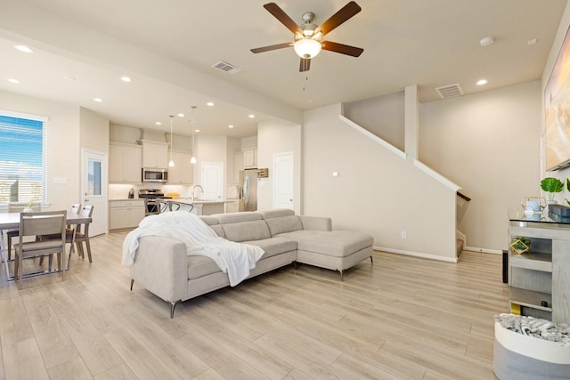 living room featuring ceiling fan, light wood-type flooring, and sink