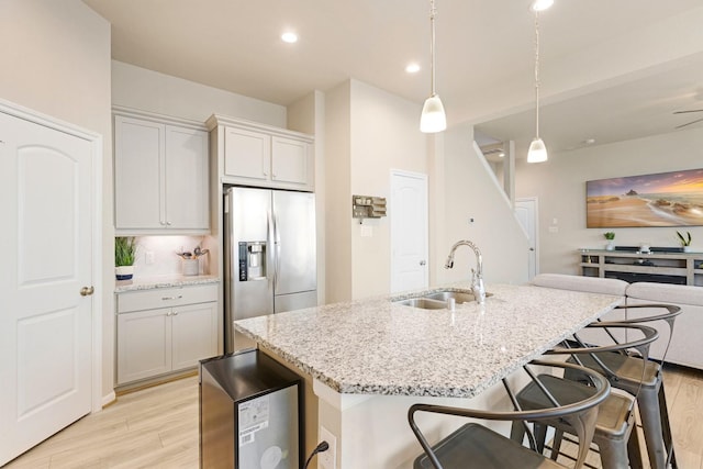 kitchen featuring light stone countertops, decorative light fixtures, an island with sink, stainless steel fridge with ice dispenser, and sink