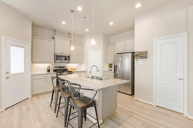 kitchen with light stone countertops, stainless steel appliances, an island with sink, a kitchen breakfast bar, and sink