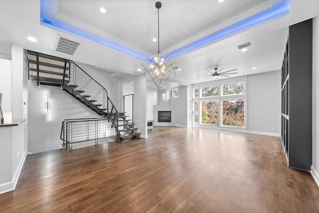 unfurnished living room featuring ceiling fan with notable chandelier, wood-type flooring, and a tray ceiling