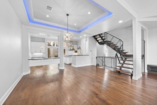 unfurnished living room with a tray ceiling, a chandelier, and dark wood-type flooring