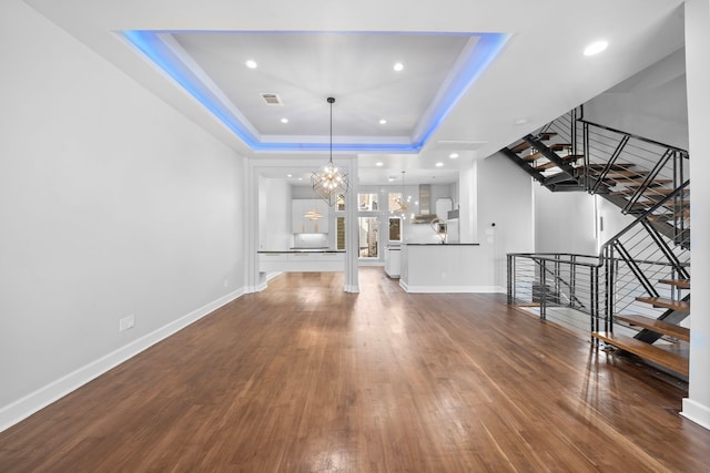 unfurnished living room with a tray ceiling, a chandelier, and dark hardwood / wood-style floors