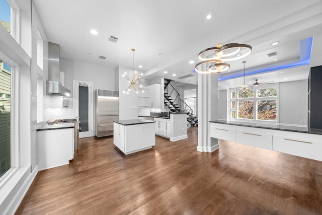 kitchen featuring white cabinets, pendant lighting, stainless steel built in refrigerator, and wall chimney range hood