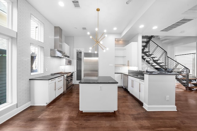 kitchen with a center island, high end appliances, dark wood-type flooring, wall chimney range hood, and hanging light fixtures