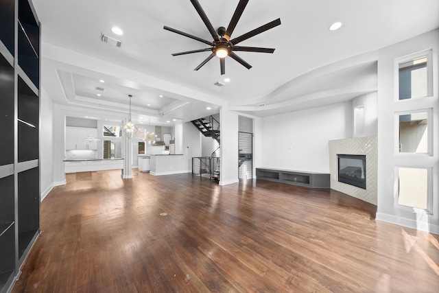 unfurnished living room featuring a raised ceiling, a fireplace, hardwood / wood-style floors, and ceiling fan with notable chandelier