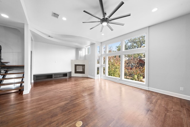 unfurnished living room with a tiled fireplace, ceiling fan, and dark hardwood / wood-style flooring