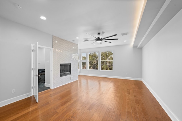 unfurnished living room featuring ceiling fan, wood-type flooring, and a tile fireplace