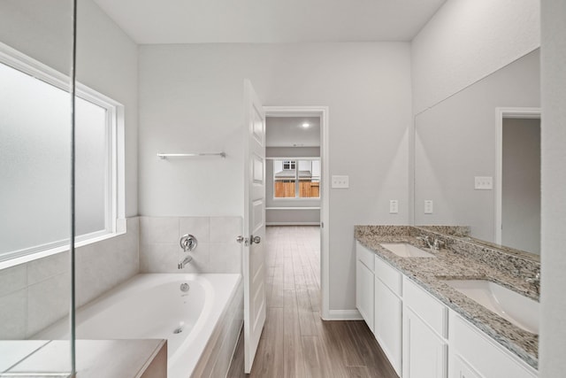 bathroom featuring double vanity, a sink, a bath, and wood finished floors