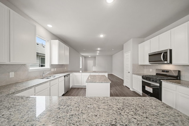 kitchen featuring appliances with stainless steel finishes, a center island, light stone countertops, white cabinetry, and a sink