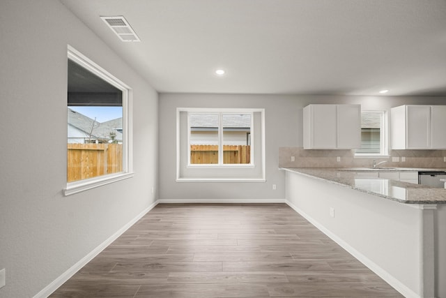 kitchen featuring light stone counters, tasteful backsplash, visible vents, white cabinetry, and a peninsula