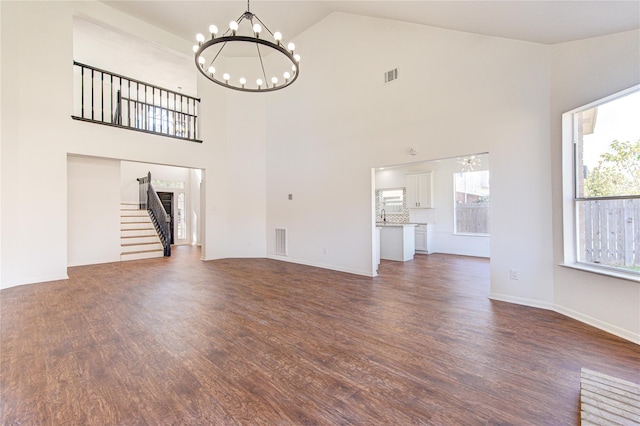 unfurnished living room with a notable chandelier, dark wood-type flooring, and high vaulted ceiling