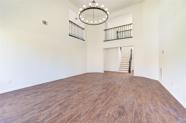 unfurnished living room featuring a towering ceiling, dark wood-type flooring, and an inviting chandelier