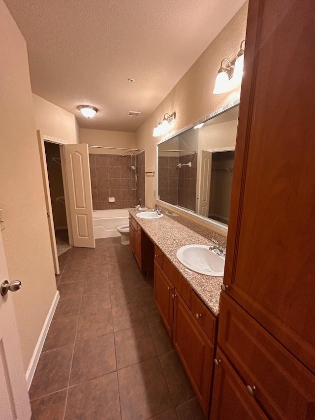 full bathroom featuring tiled shower / bath combo, tile patterned flooring, a textured ceiling, toilet, and vanity