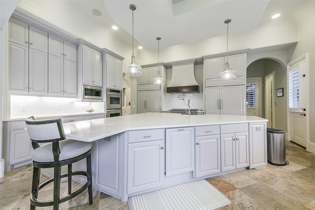 kitchen featuring a kitchen bar, premium range hood, built in appliances, hanging light fixtures, and an island with sink