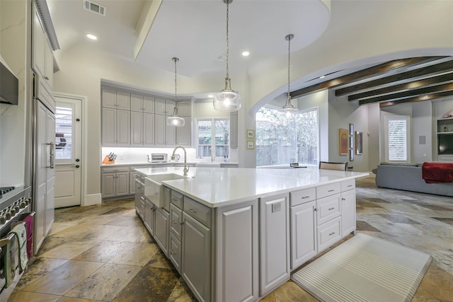 kitchen with gray cabinetry, beam ceiling, an island with sink, and pendant lighting