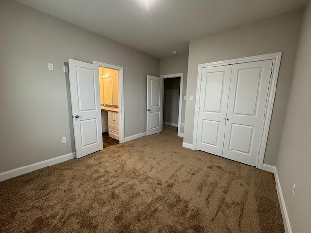 unfurnished bedroom featuring ensuite bathroom, dark carpet, and a closet