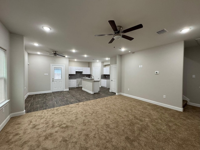 unfurnished living room featuring ceiling fan, sink, and dark carpet