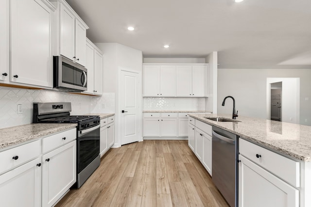 kitchen featuring sink, stainless steel appliances, a kitchen island with sink, white cabinets, and light wood-type flooring