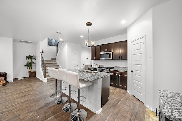 kitchen with a kitchen bar, stainless steel appliances, a kitchen island with sink, decorative light fixtures, and dark hardwood / wood-style floors