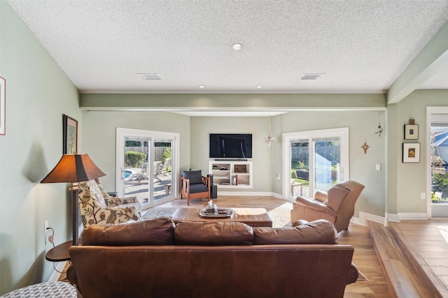 living area with light wood finished floors, baseboards, visible vents, and a textured ceiling