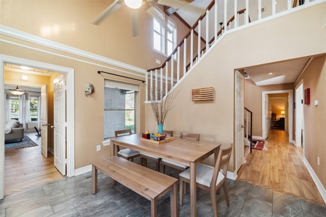 dining space featuring a towering ceiling, ceiling fan, stairs, and wood finished floors