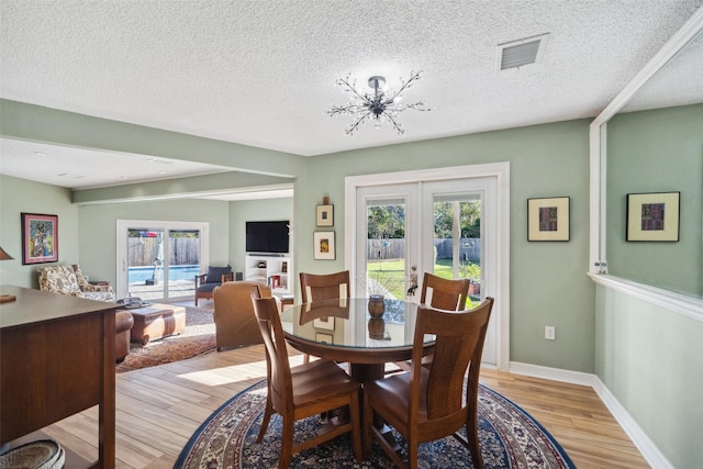 dining room with baseboards, visible vents, a textured ceiling, french doors, and light wood-style floors