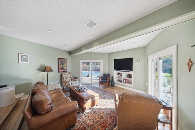 living area with visible vents, plenty of natural light, a textured ceiling, and wood finished floors