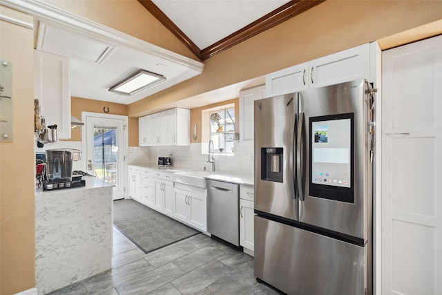 kitchen featuring tasteful backsplash, vaulted ceiling, stainless steel appliances, white cabinetry, and a sink