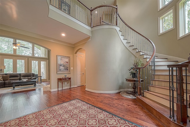 foyer entrance with hardwood / wood-style floors, ceiling fan, crown molding, and a high ceiling