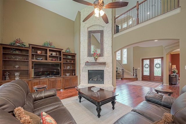 living room with french doors, ceiling fan, high vaulted ceiling, light hardwood / wood-style flooring, and a fireplace