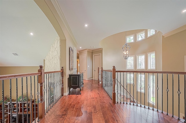 corridor with hardwood / wood-style floors, a towering ceiling, crown molding, and an inviting chandelier