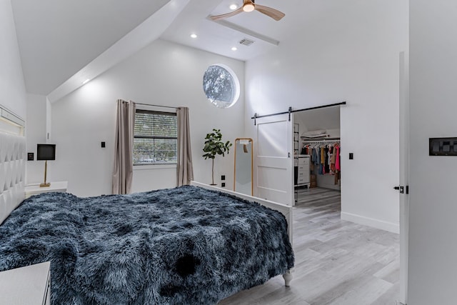 bedroom featuring ceiling fan, a barn door, light hardwood / wood-style floors, a walk in closet, and a closet