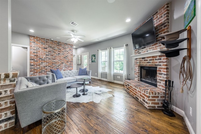 living room featuring wood-type flooring, a brick fireplace, ceiling fan, and brick wall