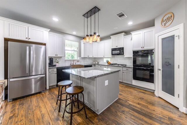 kitchen with black appliances, decorative light fixtures, a kitchen island, and dark hardwood / wood-style floors