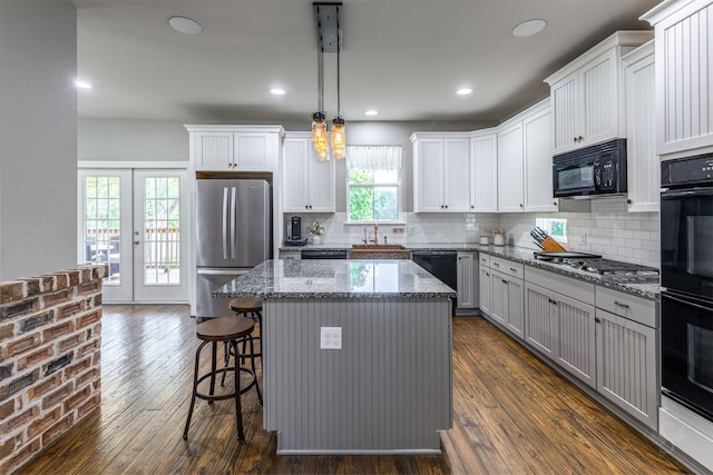 kitchen featuring pendant lighting, dark wood-type flooring, a center island, and black appliances