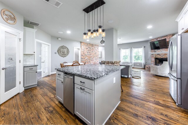 kitchen with light stone countertops, dark wood-type flooring, stainless steel refrigerator, and a kitchen island