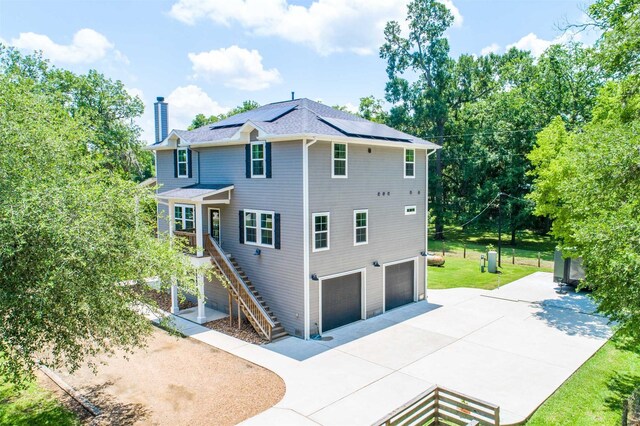 rear view of property featuring a lawn, solar panels, and a garage