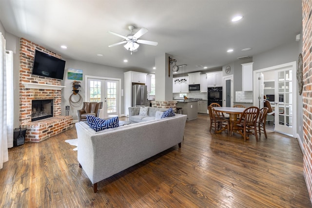 living room featuring ceiling fan, french doors, dark wood-type flooring, and a brick fireplace