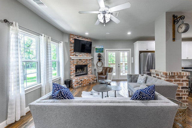 living room featuring ceiling fan, french doors, dark wood-type flooring, and a brick fireplace