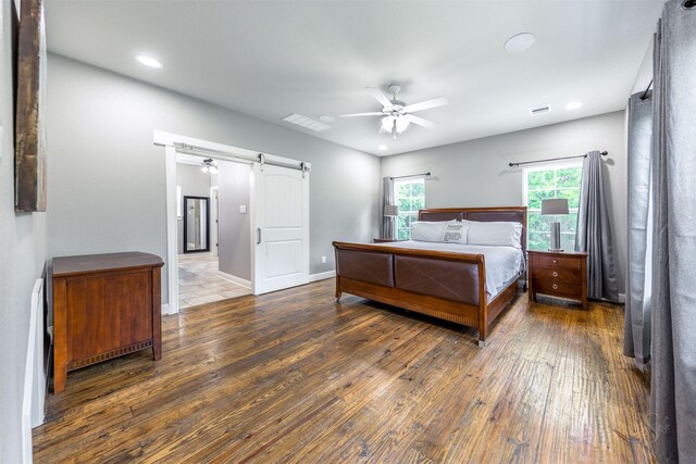 bedroom with a barn door, ceiling fan, and dark hardwood / wood-style floors