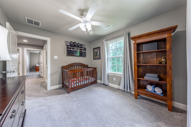 carpeted bedroom featuring ceiling fan and a crib