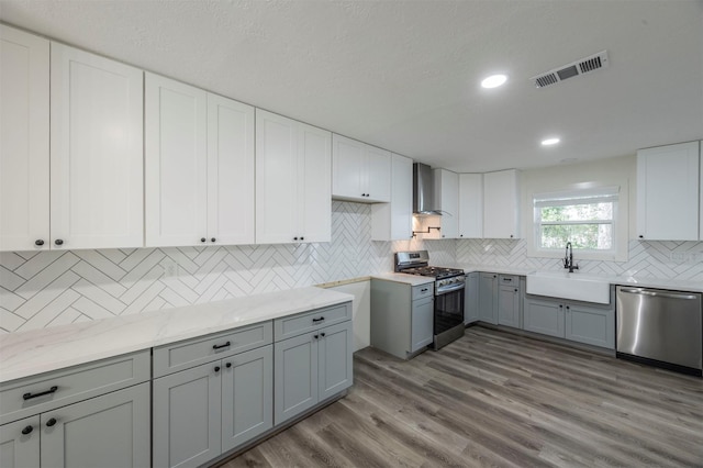 kitchen featuring light wood-type flooring, wall chimney exhaust hood, stainless steel appliances, sink, and gray cabinets