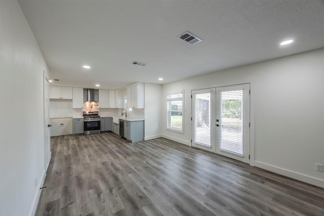 kitchen featuring french doors, wall chimney range hood, light hardwood / wood-style flooring, white cabinets, and appliances with stainless steel finishes