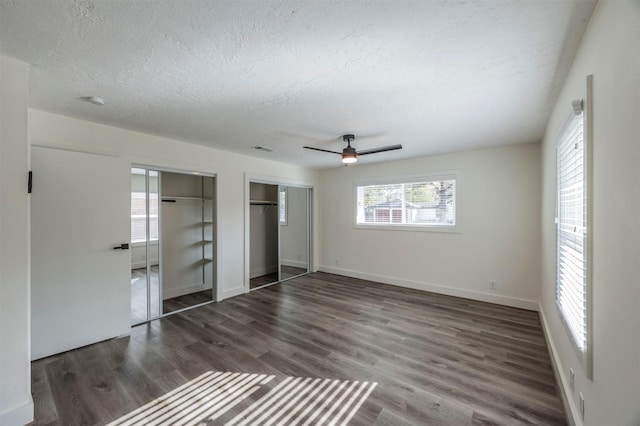 unfurnished bedroom featuring a textured ceiling, ceiling fan, dark wood-type flooring, and two closets