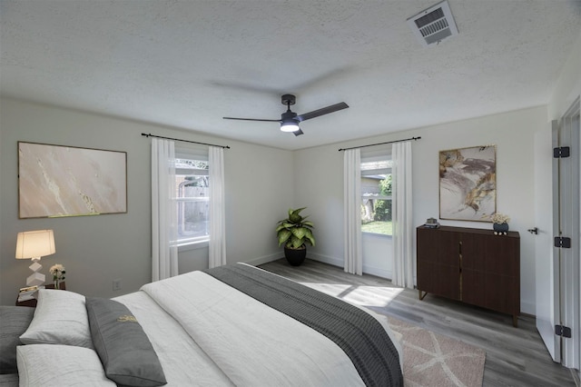 bedroom featuring multiple windows, ceiling fan, wood-type flooring, and a textured ceiling